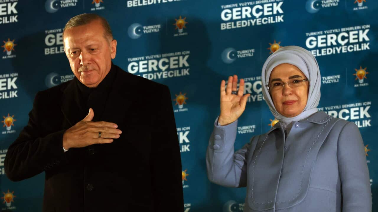 A man and a woman in formal wear gesture to a crowd